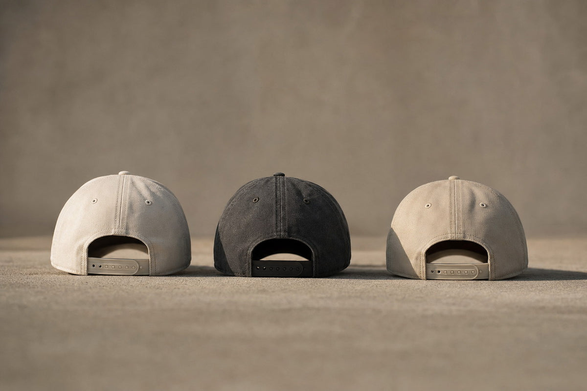 Three premium cotton canvas caps seen from behind in stone, washed black and cream — KRWN District