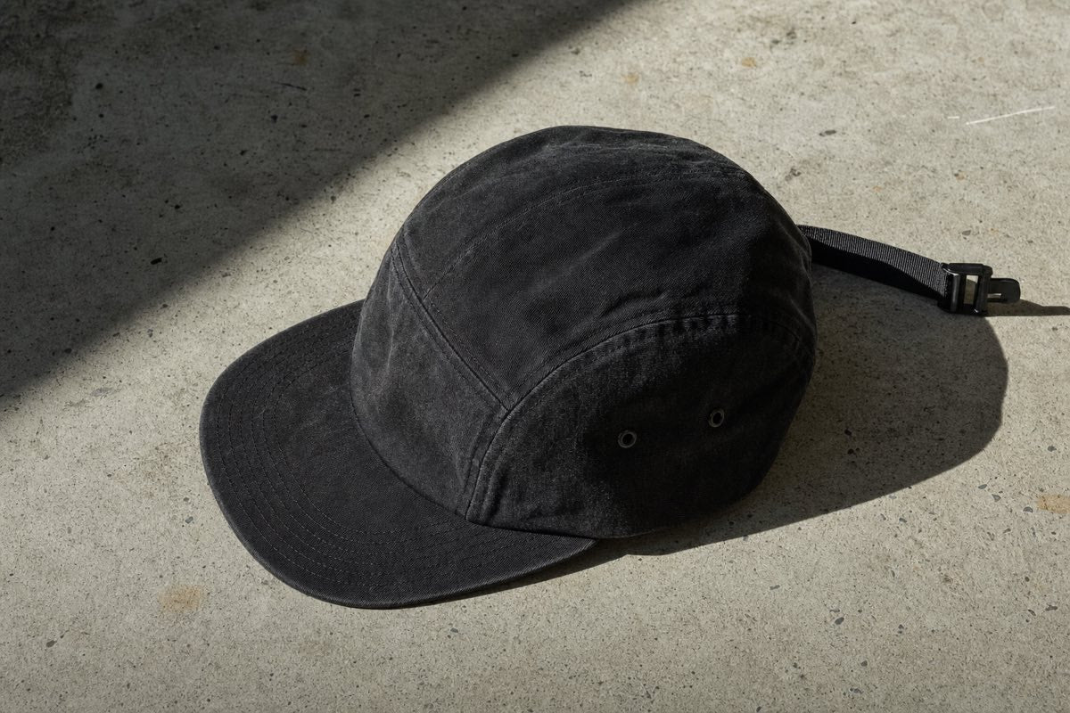 Unbranded washed black 5-panel camp cap flat lay on raw concrete