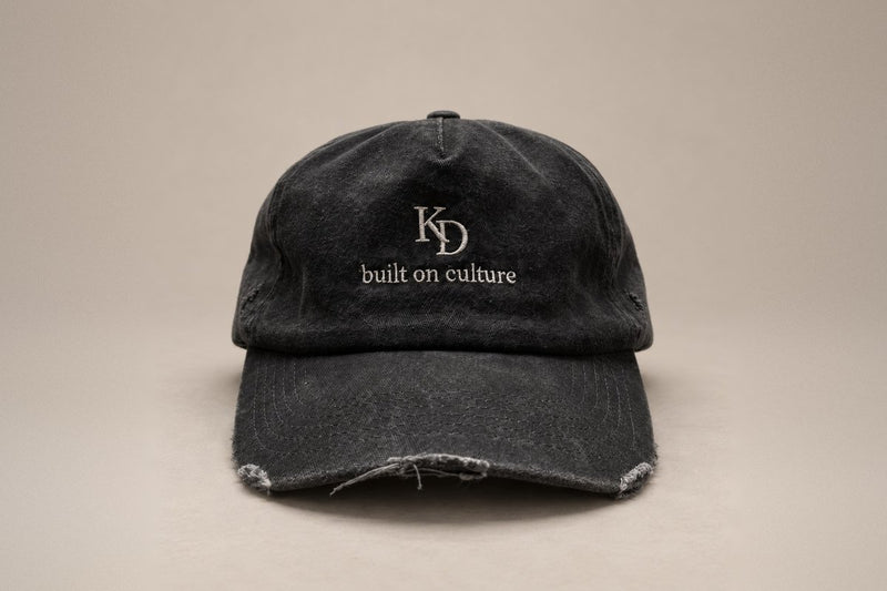 KRWN DISTRICT The Culture Washed Black: vintage 5-panel cap in stone-washed black cotton with cream KD monogram and built on culture embroidery, front view (AI-generated)