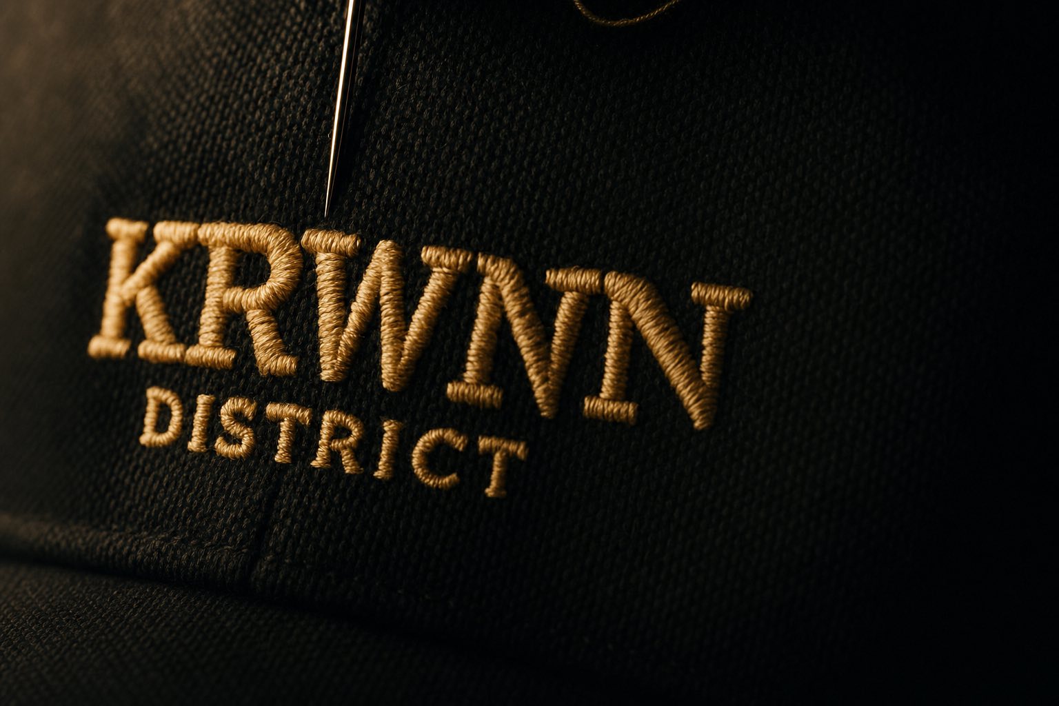 KRWN District premium streetwear cap embroidery close-up — golden cream thread on dark canvas, handcrafted detail from Rule the District '26 drop.